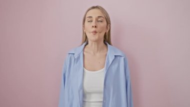 Neşeli genç sarışın kadın komik ve balık suratlı bir ifade takınıyor. Çılgın, aptal dudaklar pembe izole arkaplanda jest yapıyor. Şirin bir gömlek giyiyor, saf neşe içinde, kendinden emin bir şekilde çılgınca bir şey yapıyor..