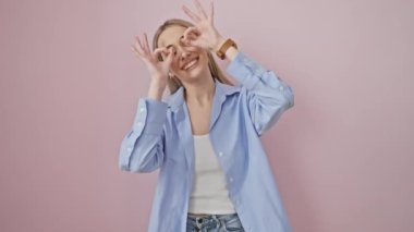 Küstah sarışın kız, dilin dışarıda, pembe arka planda parmaklarının arasından 