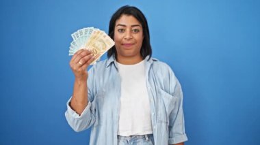 Gülümseyen orta yaşlı İspanyol kadın mavi arka planda Brezilya reais 'i tutuyor..