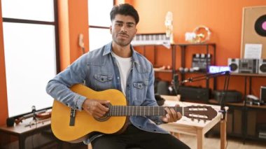 Yakışıklı İspanyol bir adam stüdyo sahnesinde akustik gitar çalıyor. Kayıt ekipmanları ve arka planda 