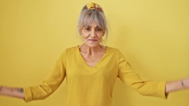 Gri at kuyruklu neşeli orta yaşlı kadın, sana ve kameraya bakıyor, izole edilmiş sarı bir arkaplana pozitif ışık saçıyor.