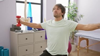 Kafkasyalı bir adam fizik tedavi kliniğinde dambıllarla egzersiz yapıyor, rehabilitasyon, zindelik ve sağlık gösteriyor..