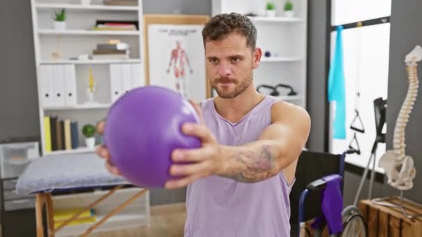 Een Gefocuste Man Een Fysiotherapie Kliniek Met Een Paarse Oefenbal — Stockvideo