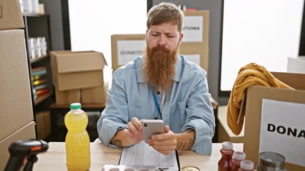 Handsome Redhead Volunteer Sitting Table Focused Smartphone Making Online Donations — Stock Video
