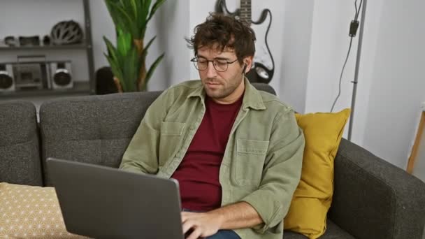 Mladý Muž Brýlemi Sluchátky Používá Notebook Gauči Uvnitř Ukazuje Ležérní — Stock video