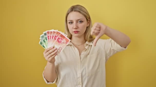怒气冲冲的金发女子在孤立的黄色背景下竖起大拇指 表示不喜欢和拒绝以色列谢克尔钞票 — 图库视频影像