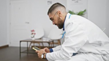 Modern bir kliniğin bekleme odasında laboratuvar önlüklü bir adam akıllı telefon kullanıyor.