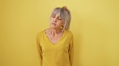 Olgun, orta yaşlı, gri saçlı, at kuyruklu, yorgun ve uykulu görünen, yorgunlukla savaşan, akşamdan kalma bakışlı bir kadın. Sarı izole arkaplandaki sabah tembelliği.