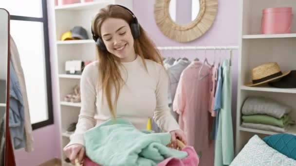 Uśmiechnięta Młoda Kobieta Słuchawkami Przegląda Ubrania Jasnej Zorganizowanej Garderobie — Wideo stockowe