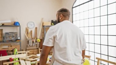 Sakallı, kendinden emin bir adam bir marangoz atölyesinde önlük takıyor..