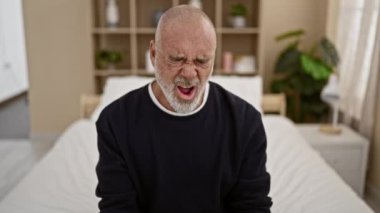 Yatak odası ortamında çeşitli duygular sergileyen sakallı olgun kel bir adam, çeşitli zihinsel durumları tasvir ediyor..