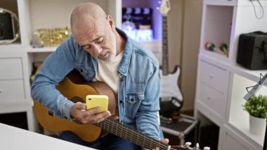 Sakallı olgun bir adam gitar çalar ve modern ofis ortamında akıllı telefon kullanır..