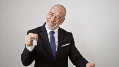 A mature man in a suit holds house keys against a white background, showcasing excitement and satisfaction.