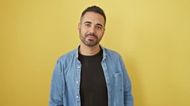 Yakışıklı, İspanyol asıllı genç bir adam. Kot gömlek içinde sevinçle poz veriyor. Neşeli bir tebessümle saçlarına dokunuyor..