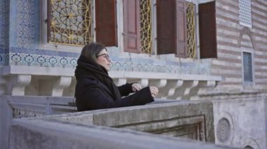 Gözlüklü düşünceli bir kadın İstanbul 'daki Topkapı Sarayı' nın tarihi mimarisinin tadını çıkarıyor.