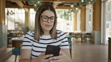 Havalı bir restoranda akıllı telefon kullanan odaklanmış bir kadın çevre aydınlatmalı ve modern dekorlu.