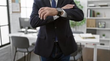 Çapraz kollu takım elbiseli profesyonel, orta yaşlı bir adam modern bir ofis içinde liderlik ve iş temalarını çağrıştırıyor..