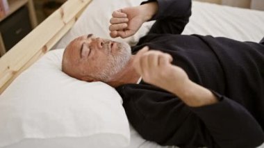 Sakallı son sınıf öğrencisi, kapalı bir yatakta uzanıyor, huzurlu ve dinleniyor görünüyor..