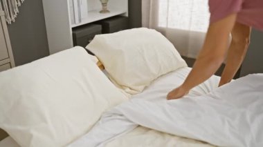 Pembe gömlekli genç bir İspanyol adam beyaz bir yatakta dinleniyor. İyi ışıklandırılmış bir yatak odasında. Huzur ve rahatlık sergiliyor..