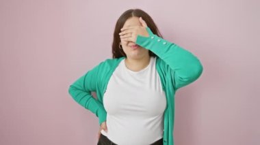 Genç, güzel İspanyol kadın. Şaşırtıcı şoku gizlemek için utangaç parmaklarından gizlice bakıyor. Pembe soyutlanmış arka planda duruyor, korku dolu gözlerini gösteriyor..