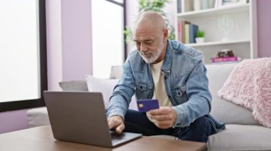 Samimi bir oturma odasında bilgisayarında kredi kartı kullanarak online alışveriş yapan sakallı son sınıf öğrencisi..