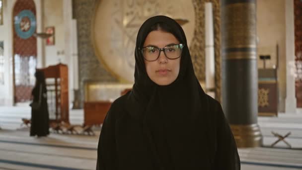 柔らかい照明の下のドーハのモスクの中のヒジャブの笑顔の若い女性は 静けさと精神性を伝えます — ストック動画