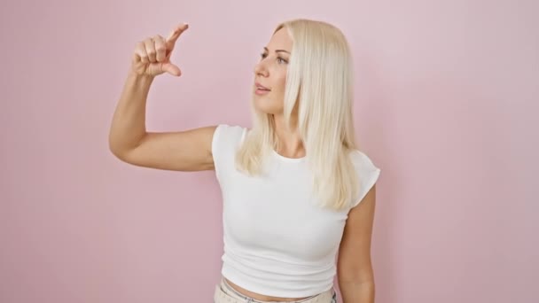 자신감 금발의 여자는 놀랍게도 그녀의 손가락으로 크기기호를 분홍색 배경에 측정의 — 비디오