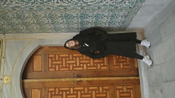 ヒジャーブの女性は タイルワークによって組み立てられた複雑に彫られた木製のドアに対して オスマンイスタンブールを呼び起こします — ストック動画