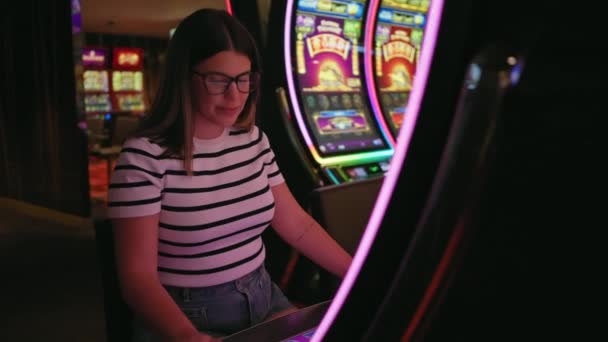笑顔の若い女性が活気に満ちたカジノでスロットマシンを演じ レジャーやエンターテイメントを体現 — ストック動画