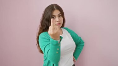 Beautiful, young hispanic woman standing, showing you the middle finger, over an isolated pink background. rude yet funny fuck off expression, naughty impolite attitude on show.