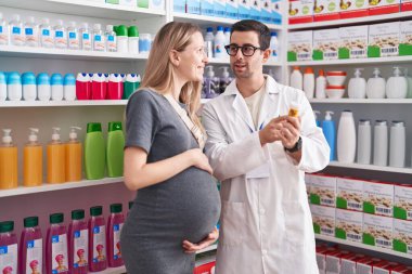 Kadın ve erkek eczacı ve hamile müşteri eczanede ilaç şişesi tutuyorlar.