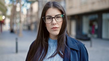 Young hispanic woman standing with serious expression at street