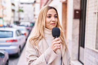 Young blonde woman reporter working using microphone at street