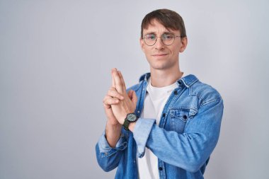 Beyaz, sarışın, gözlüklü, el hareketleriyle sembolik bir silah tutan, cinayet silahlarıyla oynayan, kızgın yüzlü bir adam. 