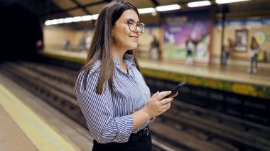 Madrid metro istasyonunda akıllı telefon kullanan güzel İspanyol bir kadın metroda bekliyor.
