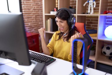 Orta yaşlı İspanyol kadın kulaklık takarak video oyunu oynuyor. Çok mutlu ve heyecanlı. Kolları havada, gülümseyerek ve başarı için çığlık atarak kazanan jestler yapıyor. kutlama konsepti. 