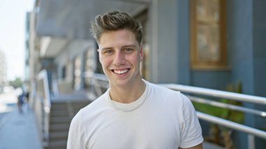 Kendinden emin, sportif görünümlü beyaz bir adam şehrin açık alanındaki hareketli bir caddede gülümseyerek pozitiflik, neşe ve rahat bir hava yayarken yakalandı..