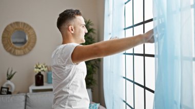Genç bir İspanyol adam perdeleri parlak, şık bir oturma odasına yerleştiriyor, ev ve rahatlama hissi uyandırıyor..