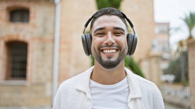 Akdeniz caddesinde gülümseyen kulaklıklı yakışıklı sakallı adam.