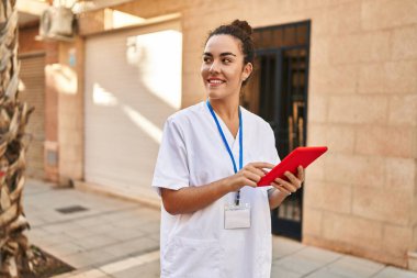 Young beautiful hispanic woman physiotherapist smiling confident using touchpad at street