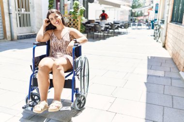Young beautiful hispanic woman smiling confident sitting on wheelchair at street