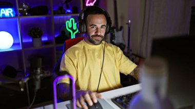 Sarı tişörtlü İspanyol bir adam evde neon ışıkları olan süslü bir odada oyun oynuyor..