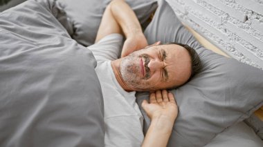 Yorgun, orta yaşlı, gri saçlı, rahat bir şekilde yatak odasında dinlenen, yumuşak yatağında dinlenen, mışıl mışıl uyuyan, sabah koşusundan kaçan bir adam..