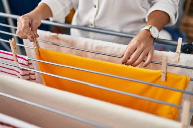 Young beautiful hispanic woman hanging clothes on clothesline at laundry room