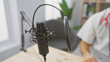Blurred hispanic man with beard standing behind a studio microphone, suggesting a podcast or radio recording session. clipart