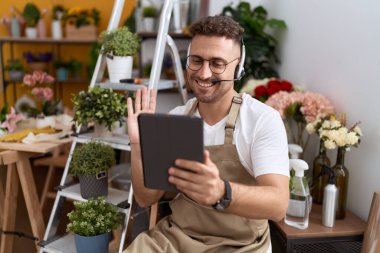 Hispanic man with beard working at florist shop doing video call looking positive and happy standing and smiling with a confident smile showing teeth 