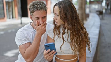 Meraklı bir adam ve özenli bir kadın, modern şehir yaşamını tasvir eden bir şehir caddesinde akıllı telefonu birlikte inceliyor..