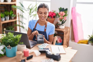 Young beautiful hispanic woman florist using laptop and data phone at florist