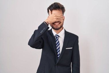 Dövmeli, takım elbiseli, kravatlı, gülümseyen ve gülümseyen genç İspanyol bir adam, şaşırmak için gözlerini kapatıyor. kör kavram. 