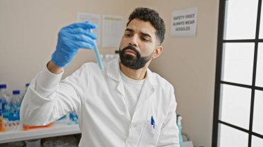 Laboratuvar önlüklü İspanyol bir adam araştırma tesisinde kapalı bir deney tüpünü inceliyor..